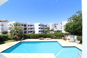 Ein Swimmingpool mit Liegestühlen, einer Palme und weißen Gebäuden im Hintergrund.