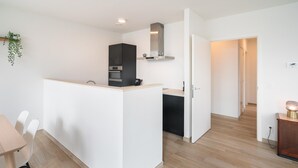 A modern kitchen with a built-in oven, a microwave, and a black cabinet. There is a wooden dining table with chairs. The room has light wooden flooring and white walls. - Spacious Apartment for 8 Guests (Antwerp)