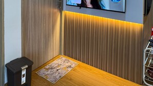 A modern room with a television mounted on a wall, a wooden door, and a small trash bin. - 2-bedroom apartment in Bandar Lampung with Mall Access (Bandar Lampung)