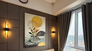 A modern living room with a sectional sofa, a wall-mounted clock, and a painting. - 2-bedroom apartment in Bandar Lampung with Mall Access (Bandar Lampung)