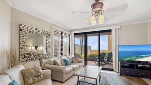 Ein Wohnzimmer mit einer Couch, einem Couchtisch, einem Fernseher und einem Balkon mit Stühlen.