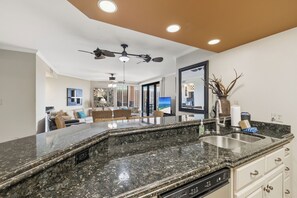 A kitchen with granite countertops, a dishwasher, and a ceiling fan. - Four Seasons 101E by Liquid Life (Orange Beach)