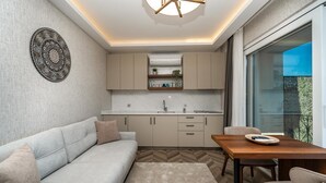 Una cocina moderna con horno empotrado, una zona de comedor con mesa y sillas de madera, un sofá y un amplio ventanal con vistas.