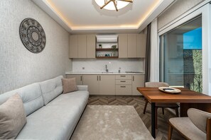 Une cuisine moderne dotée d’un four encastré, un coin repas avec une table et des chaises en bois, un canapé et une grande fenêtre offrant une vue dégagée.