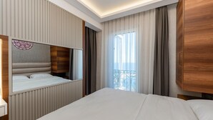 Habitación de hotel con cama, mesita de noche, espejo, armario y ventana con cortinas.