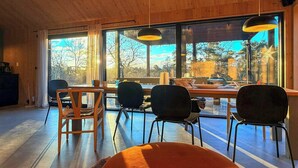 Un intérieur moderne avec un plafond en bois, de grandes fenêtres et un coin repas comprenant des chaises et une table.
