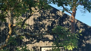 Un bâtiment en bois avec une entrée dotée d’une porte en verre, entouré d’arbres et d’un sol en gravier.