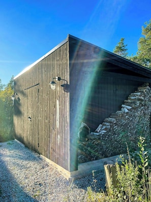 A wooden building with a gravel driveway and a stack of logs. - Architect-designed house in Etelhem, Gotland (Stånga)