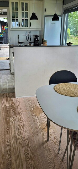 Eine moderne Küche mit weißen Schränken, einem Kühlschrank und einem Essbereich mit einem runden Tisch und Stühlen.