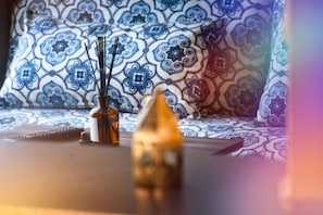 Ein Zimmer mit gemusterten Kissen, einer Flasche mit schwarzen Stäbchen und einem kleinen Dekorationsgegenstand auf einem Tisch.