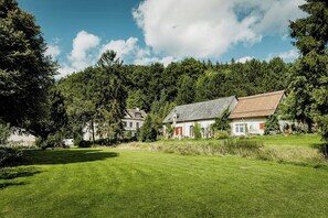 Ett hus med ett rött tak och vita väggar, omgivet av en gräsklädd äng och täta träd.