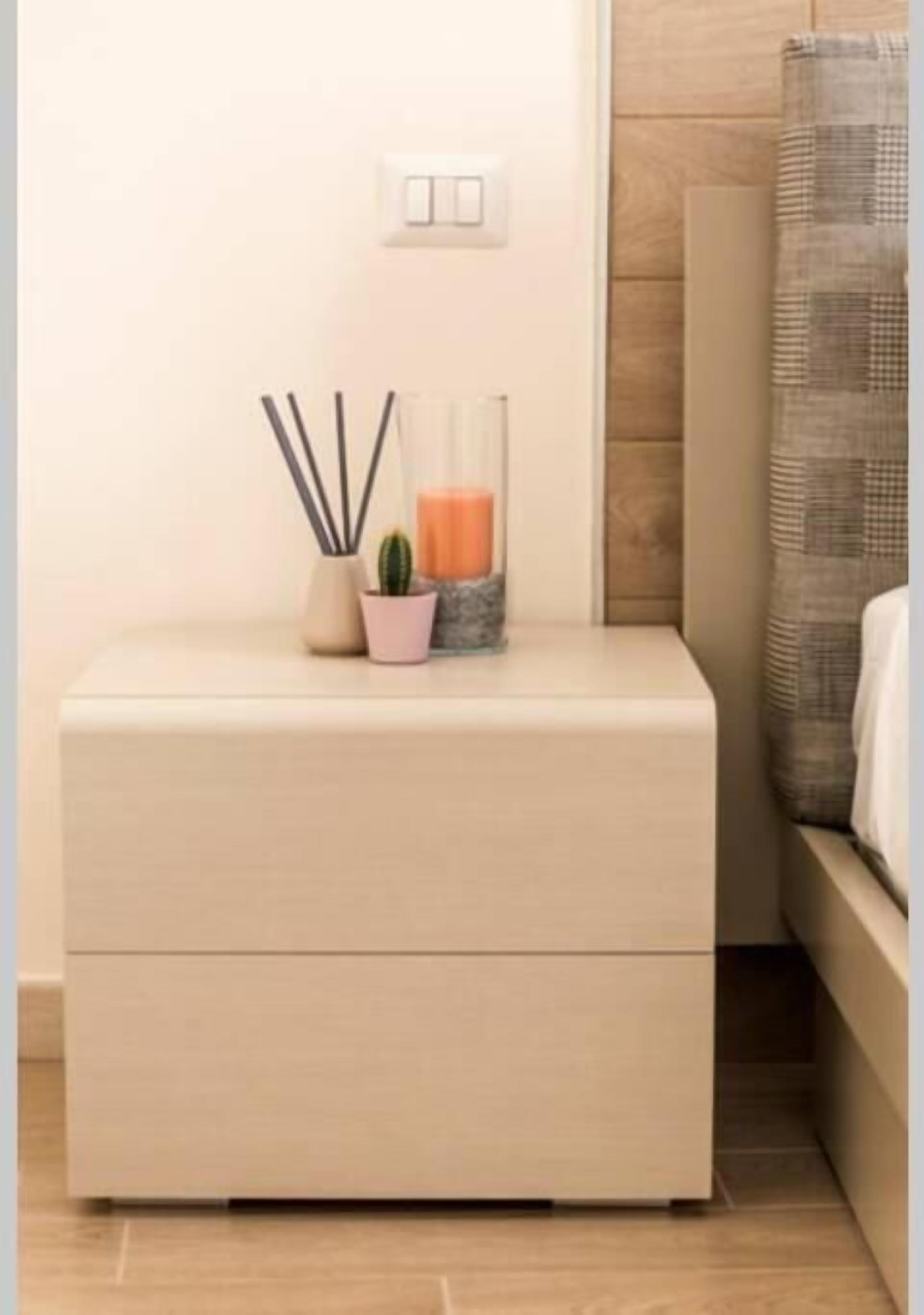 A minimalist bedside table with a drawer, a small potted plant, a candle, and a glass container.
