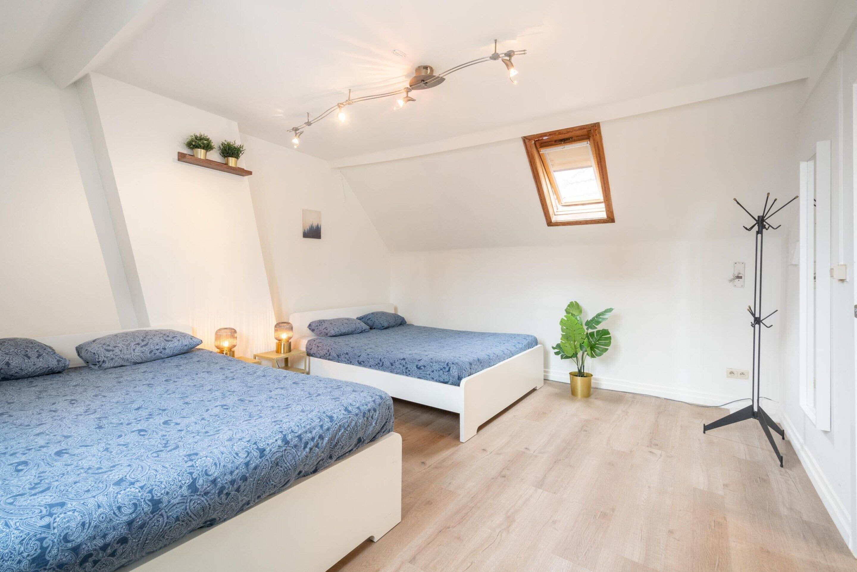 A bedroom with two beds, a ceiling light fixture, a window, and a floor lamp.