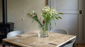 A dining table with a rustic wooden top, surrounded by white chairs, in a room with a white door and a black pipe on the wall. - Noble residence with pool in the Langhe (Cherasco)