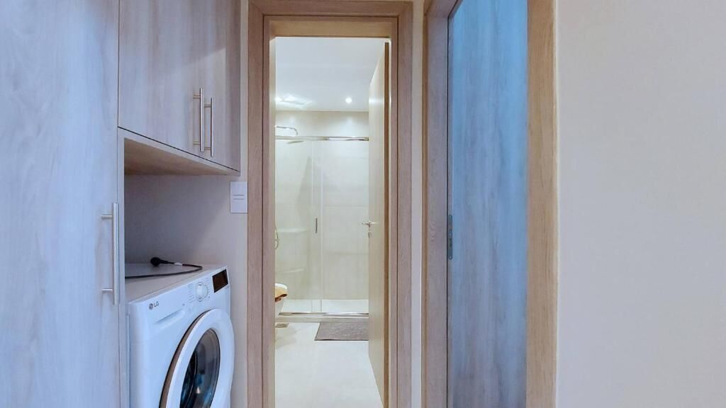 Un área de lavandería con lavadora, un baño con ducha y un marco de puerta de madera.
