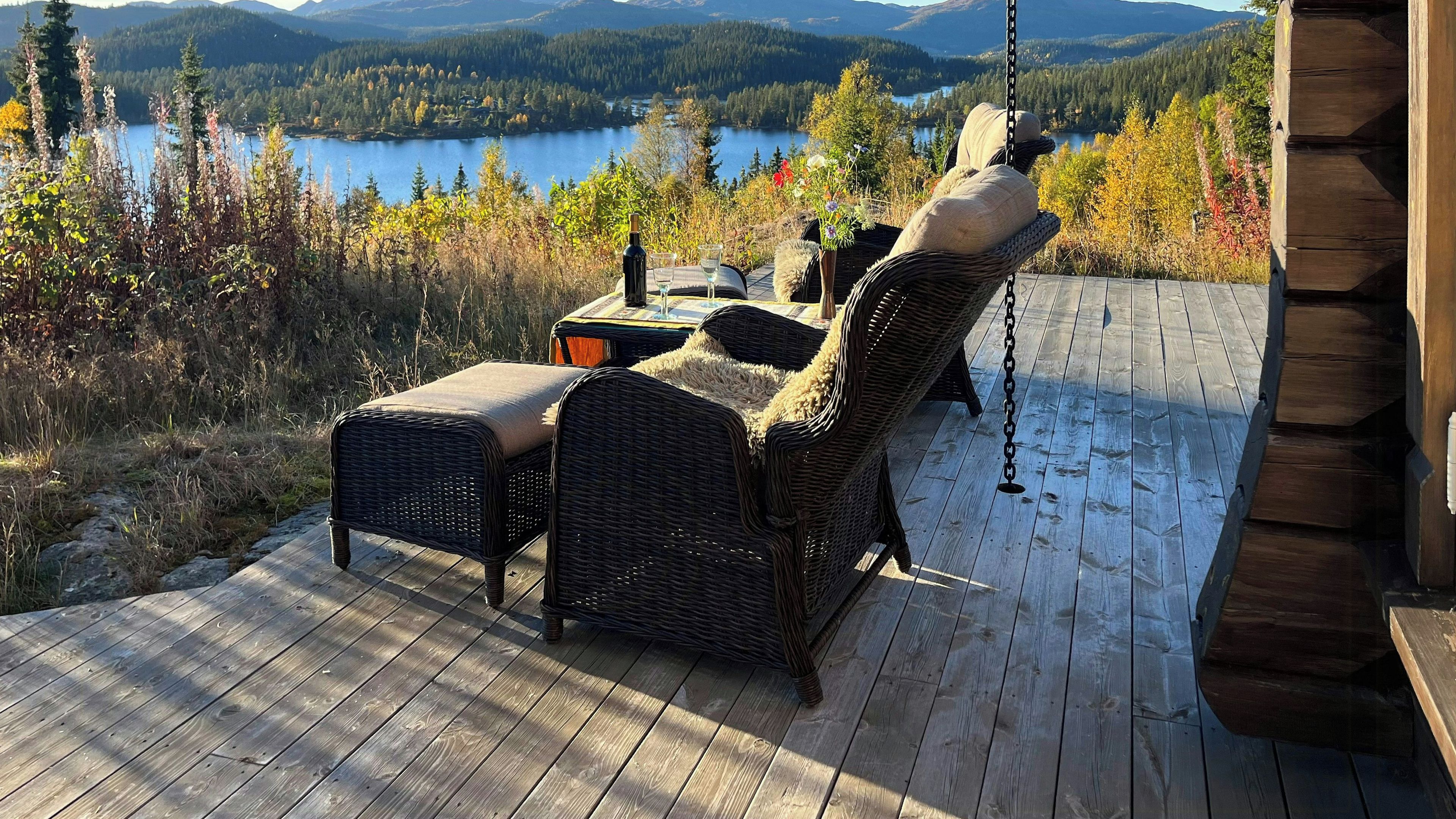 A wooden deck with wicker furniture overlooking a lake and forested mountains.
