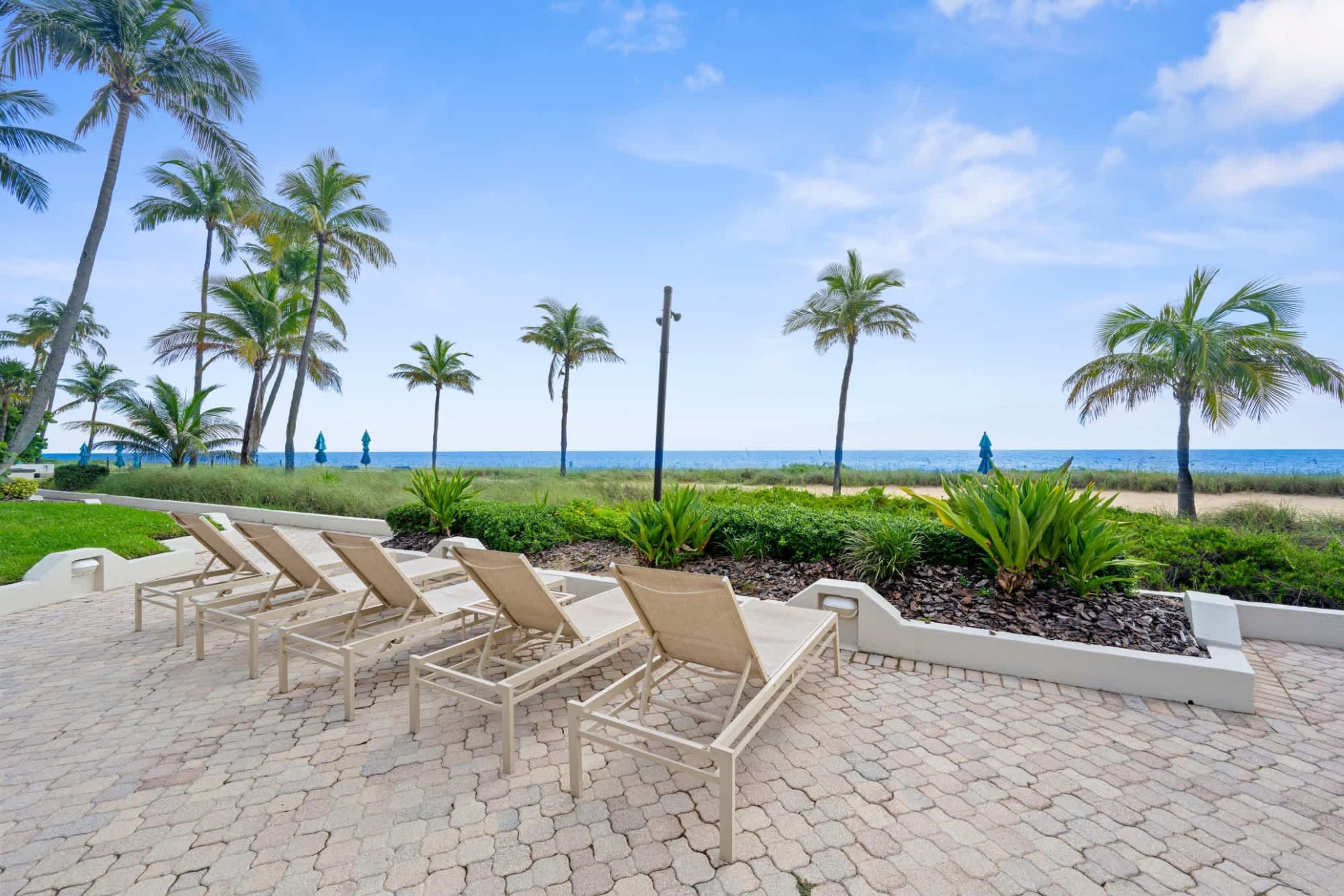 Un área pavimentada con sillones de descanso y palmeras, con vista a una playa.