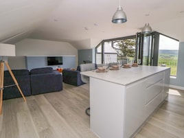 Una cocina moderna con una isla central, un comedor con mesa para cuatro, un sofá y una televisión en la sala.