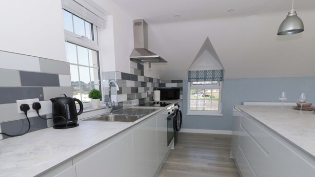 A modern kitchen with a built-in washing machine, a kettle, and a window with a view. - Rosemary Cottage 2 (Tywyn)