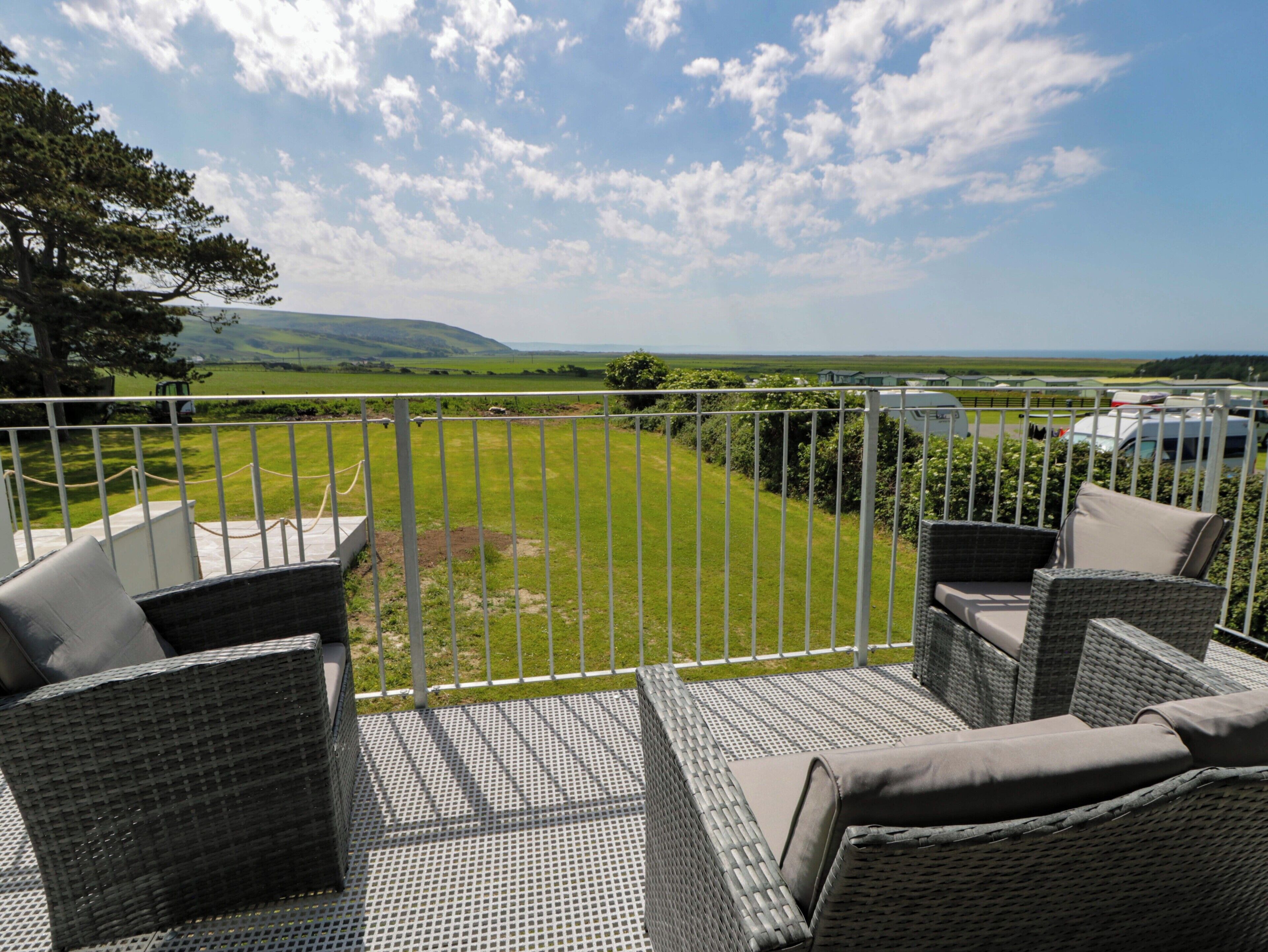 A balcony with wicker furniture overlooking a grassy yard and distant hills.