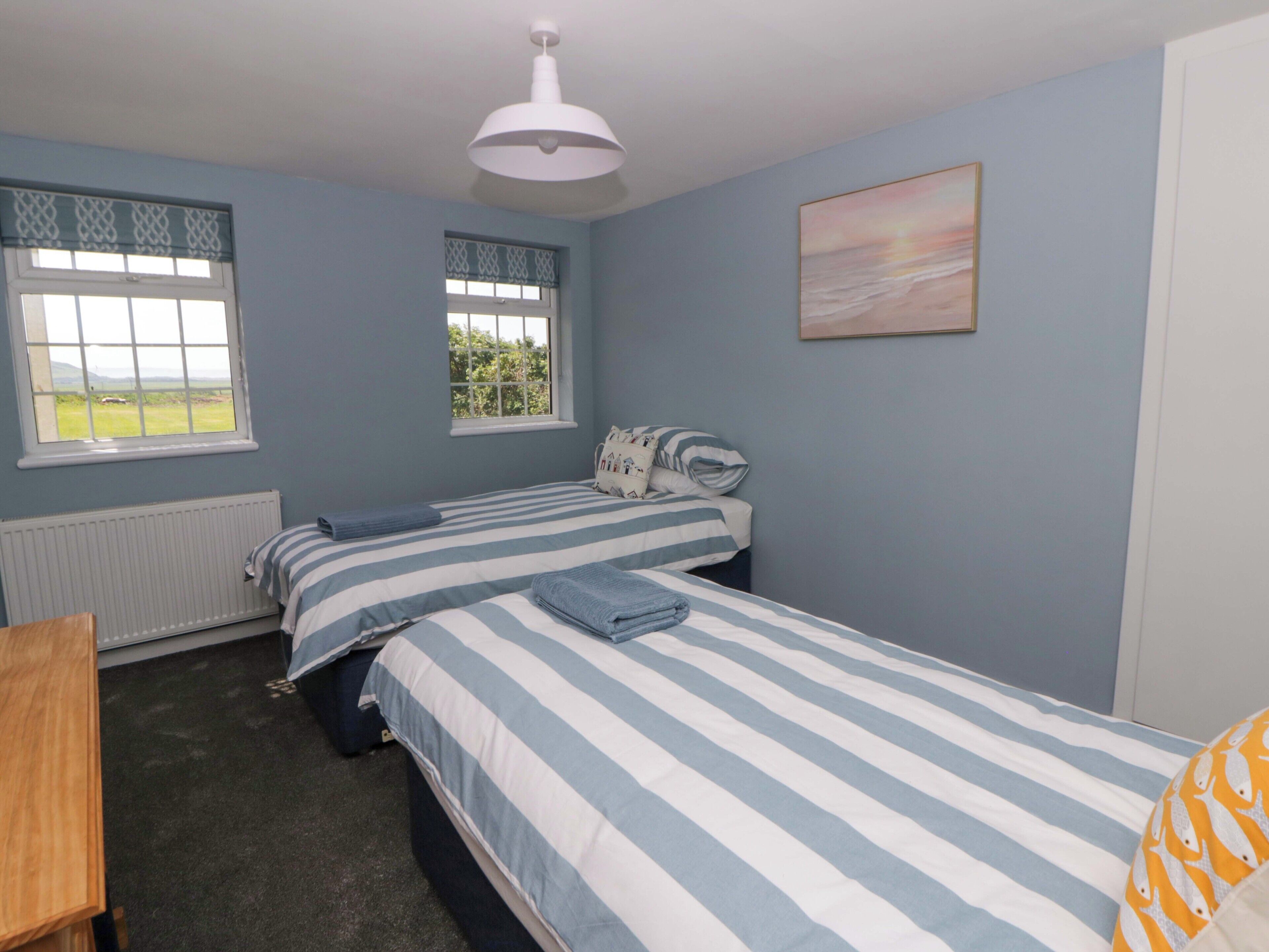 A bedroom with two beds, a window, a radiator, and a painting on the wall.