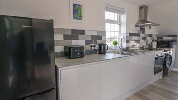 Una cocina moderna con refrigerador, tostadora, hervidor, lavamanos, microondas y lavadora.