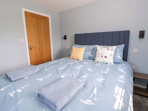 A bedroom with a bed, pillows, a wooden door, and a headboard. - Rosemary Cottage 2 (Tywyn)