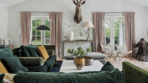 A living room with a mounted deer head, green sofas, a white table, and a window with curtains.