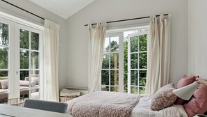 A bedroom with a bed, a table, and a view of greenery outside.
