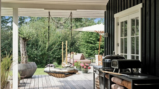 A wooden deck with a hanging chair, a grill station, and a large planter.