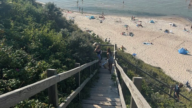 A wooden staircase leading to a beach with clear water and people.