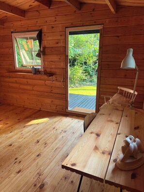 Interior de una cabaña de madera con un ventanal grande, una mesa y una lámpara.