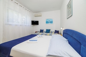 Ein Hotelzimmer mit Bett, Fernseher, einem Bild an der Wand und einem Fenster mit Vorhängen.