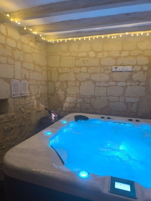 Una stanza dalle pareti in pietra con una vasca idromassaggio illuminata da luci LED blu.