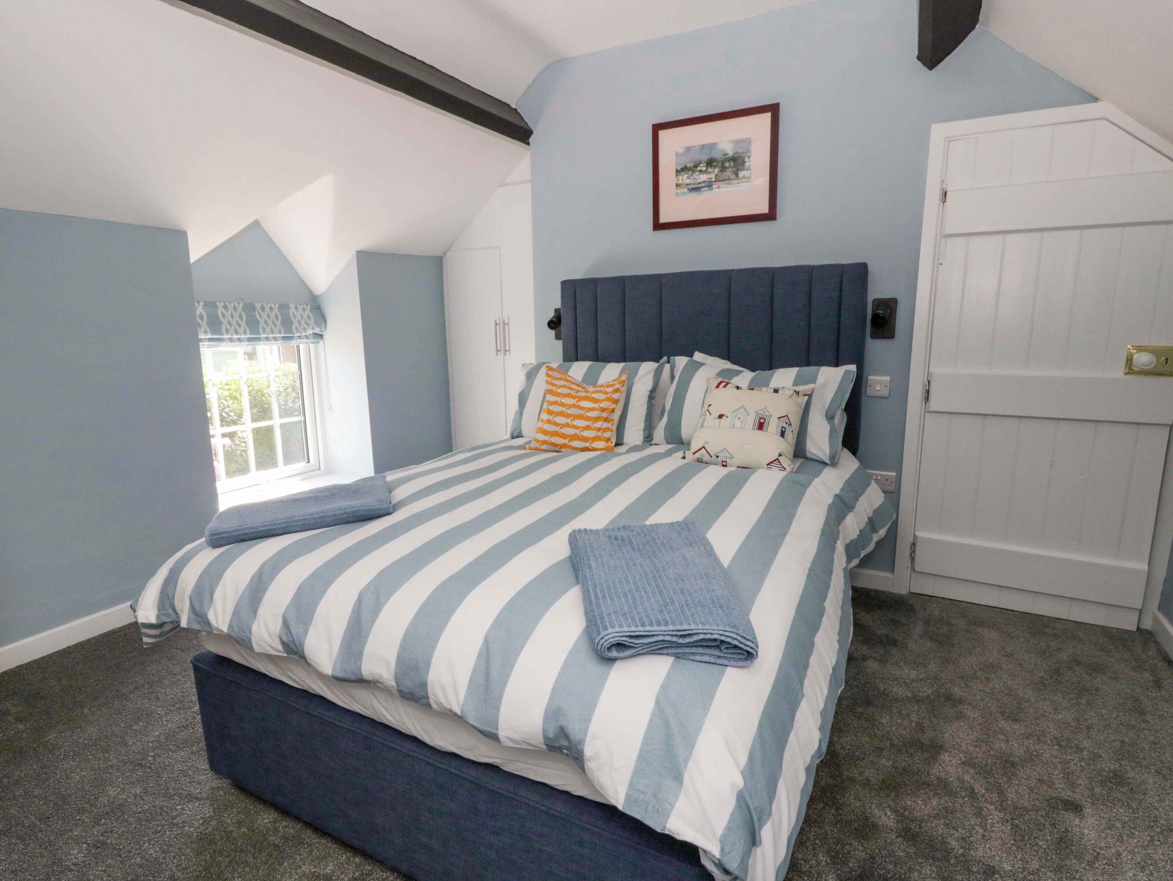 Quarto com cama, janela, porta e um quadro na parede.