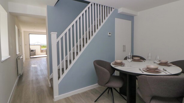 A dining area with a round table, chairs, and a staircase. - Rosemary Cottage 1 (Tywyn)