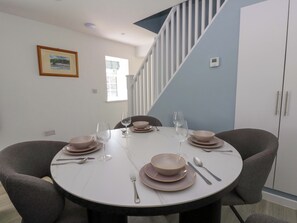 A dining area with a round table set for four, chairs, and a staircase in the background. - Rosemary Cottage 1 (Tywyn)