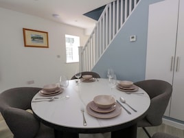 Un comedor con una mesa redonda dispuesta para cuatro personas, sillas y una escalera al fondo.