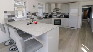 A modern kitchen with a central island, built-in appliances, and a view to the outside. - Rosemary Cottage 1 (Tywyn)