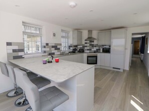 A modern kitchen with a central island, built-in appliances, and a view to the outside. - Rosemary Cottage 1 (Tywyn)
