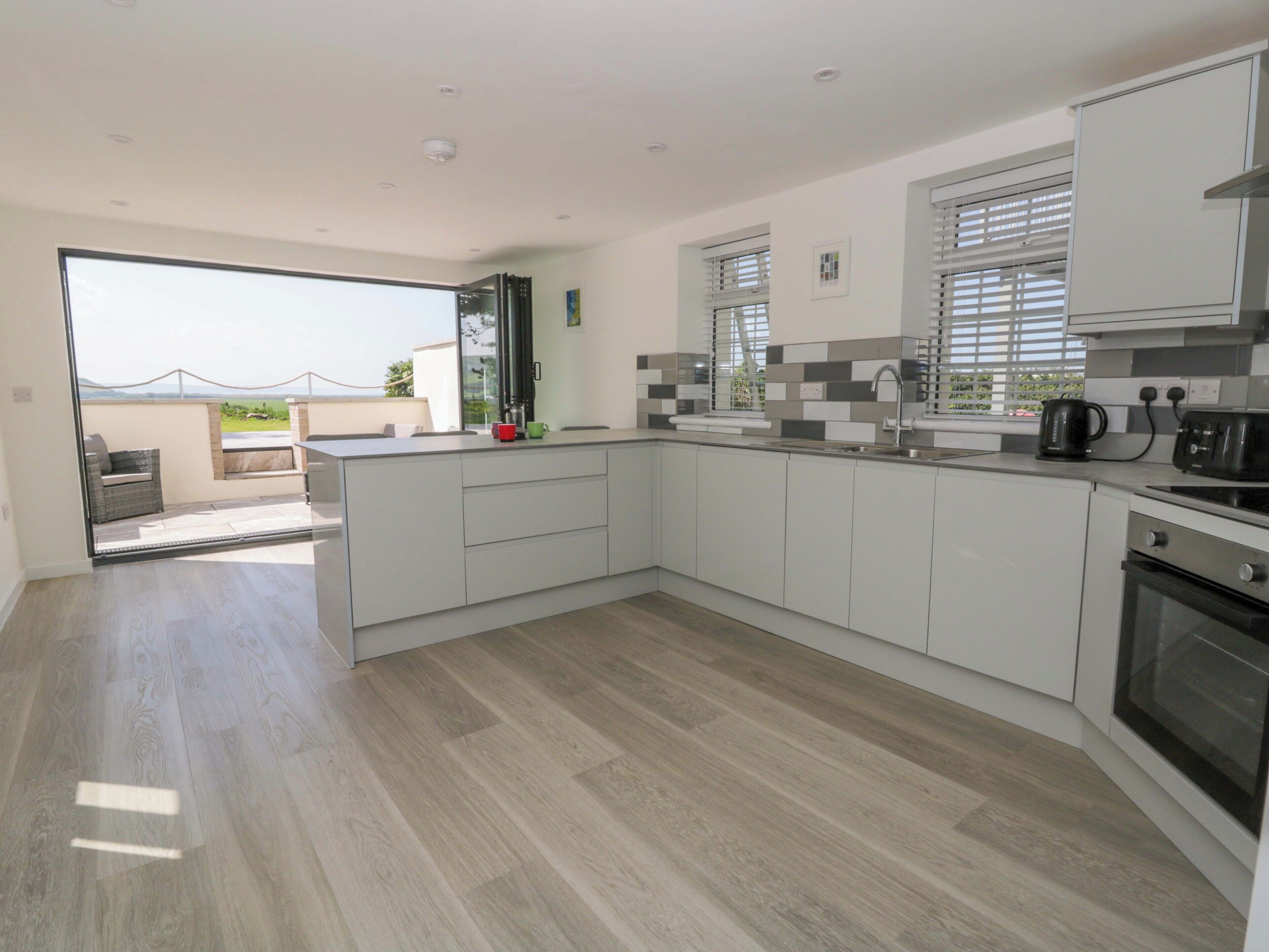 A modern kitchen with white cabinetry, a built-in oven, and a large window with blinds.