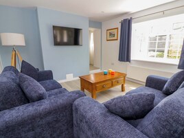 Un salón con sofás azules, una mesa de centro de madera, un televisor de pantalla plana y una ventana con cortinas.