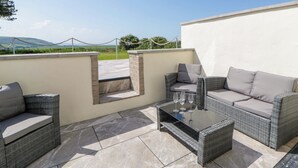 An outdoor patio with wicker furniture, a glass-top table, and a view of the countryside. - Rosemary Cottage 1 (Tywyn)