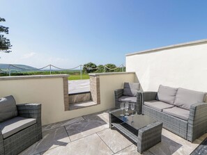 An outdoor patio with wicker furniture, a glass-top table, and a view of the countryside. - Rosemary Cottage 1 (Tywyn)