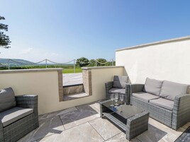 Un patio al aire libre con mobiliario de mimbre, una mesa de vidrio y vistas al campo.