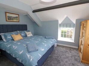 A bedroom with a bed, a window with a view, a painting on the wall, and a wardrobe. - Rosemary Cottage 1 (Tywyn)