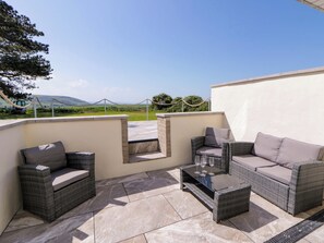 An outdoor patio with wicker furniture, a glass-top table, and a view of the countryside. - Rosemary Cottage 1 (Tywyn)