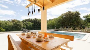 Ein Holztisch für das Frühstück gedeckt, mit einem Pool im Hintergrund.