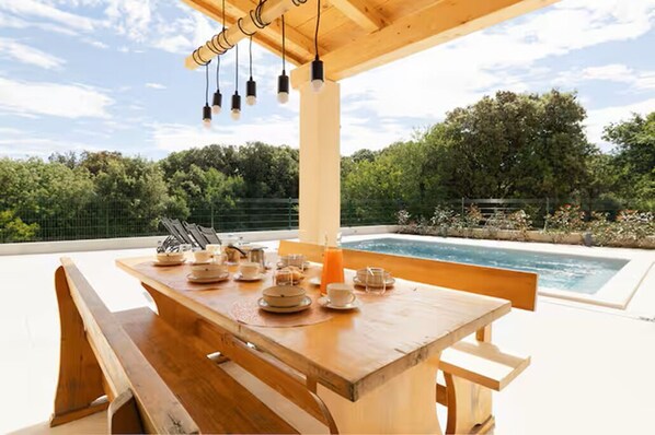 A wooden dining table set for breakfast with a pool in the background. - Villa Nati - Enjoyable 3-bedroom house with pool (Pula)