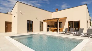 Ein modernes Haus mit Swimmingpool, einer Terrasse mit Stühlen und einem überdachten Außenbereich.